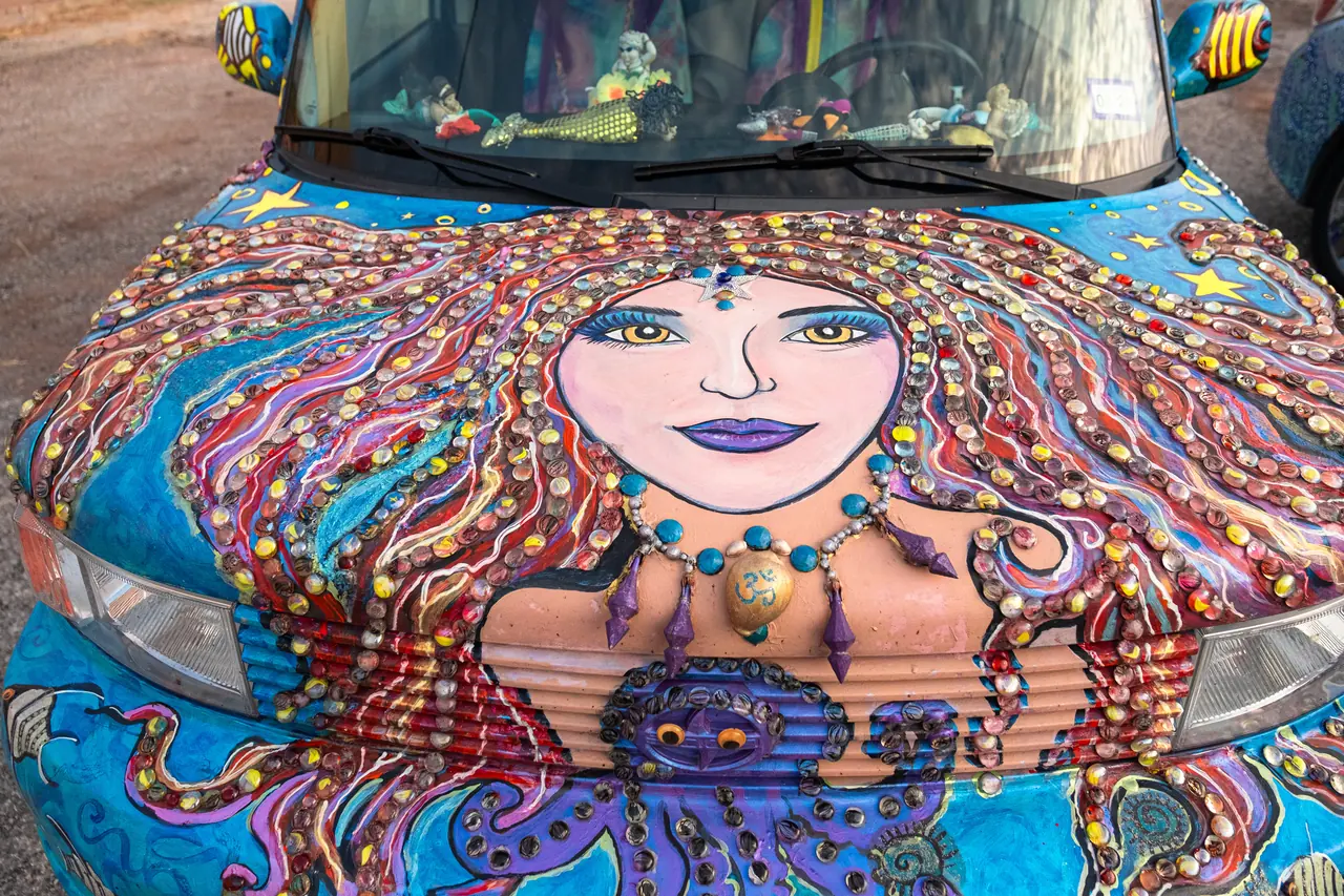 The hood of a car painted with a smiling mermaid with beaded hair and an octopus, with fish painted on the mirrors.