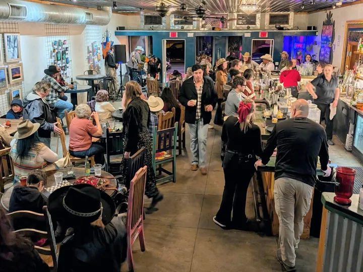 Inside Alcove Social: guests at tables and along the counter, with framed art on the walls.