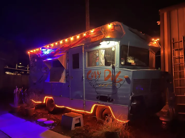 The Cowdog food truck at night, outlined in orange lights under strings of bulbs.
