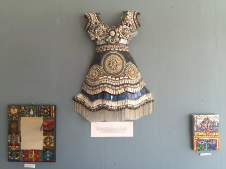 A dress-shaped mosaic of tile, beads and glass on a gallery wall at Galeria Sibley, between two smaller mosaics.